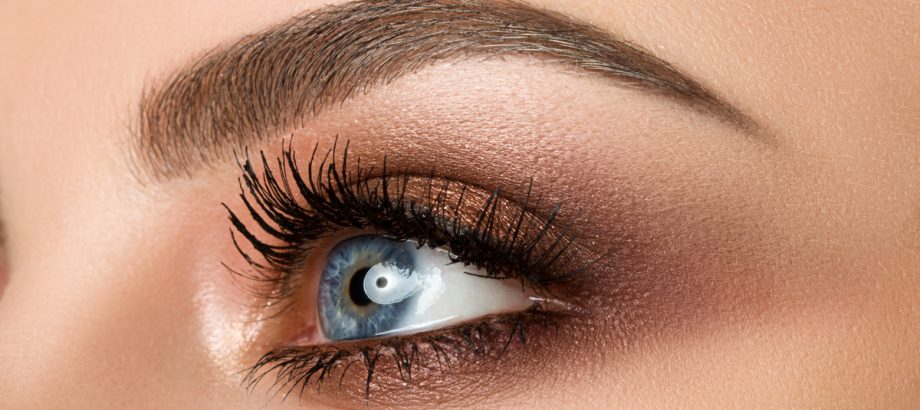 Close up of blue woman eye with beautiful brown with red and orange shades smokey eyes makeup. Modern fashion make up.